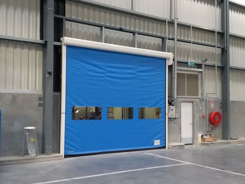 Blue high speed roll door with vision panels installed in a warehouse.